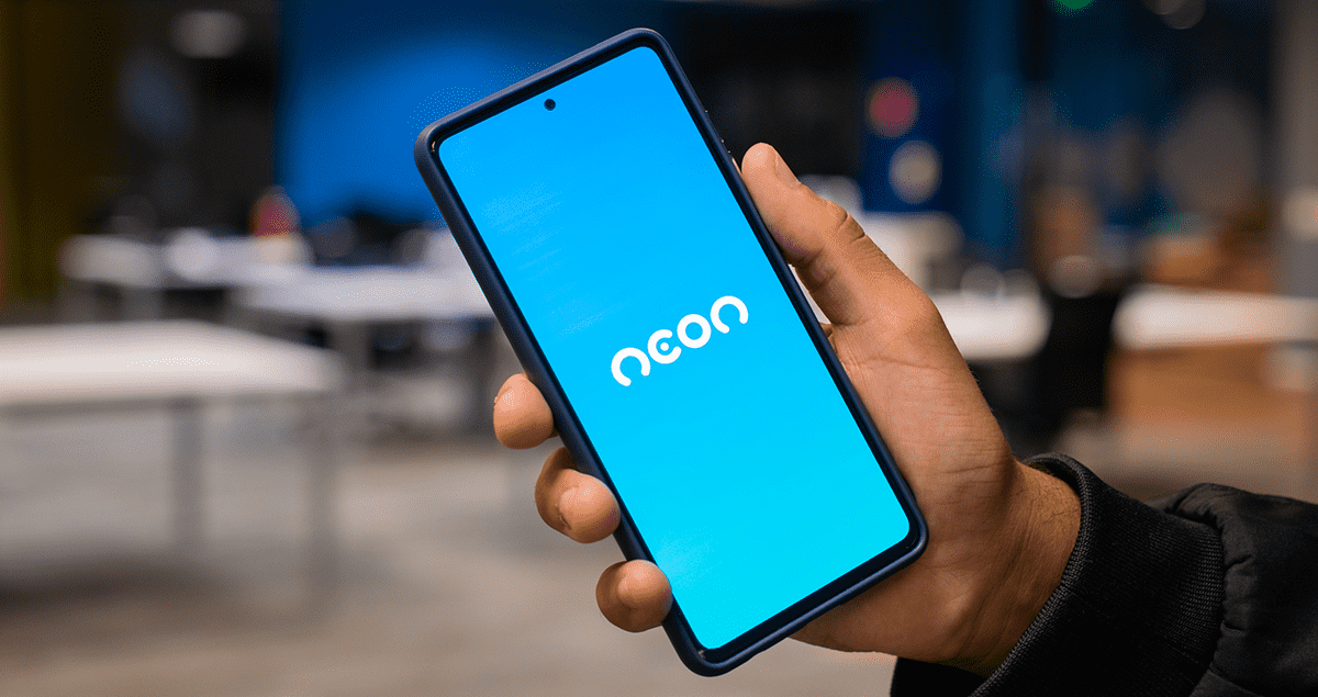 Neon: nossa história, produtos, dia a dia e curiosidades 1 Mão segurando celular com o logo Neon na tela sobre fundo azul