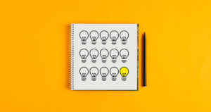 Caderno com lâmpadas desenhadas e caneta ao lado sobre fundo amarelo