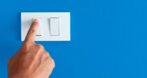 Pessoa apertando interruptor branco sobre fundo azul