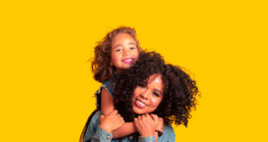 Mulher com criança abraçada, ambas sobre fundo amarelo
