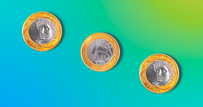 Três moedas de um real alinhadas na diagonal sobre fundo azul