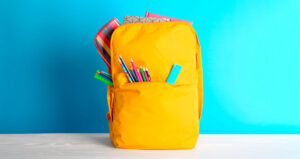 Mochila amarela sobre fundo azul com diversos lápis de cor para fora do bolso