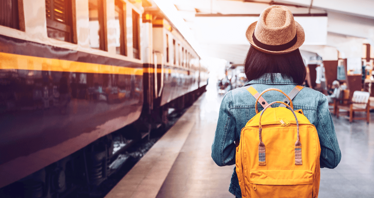Mulher com chapéu e mochila ao lado de trem em estação