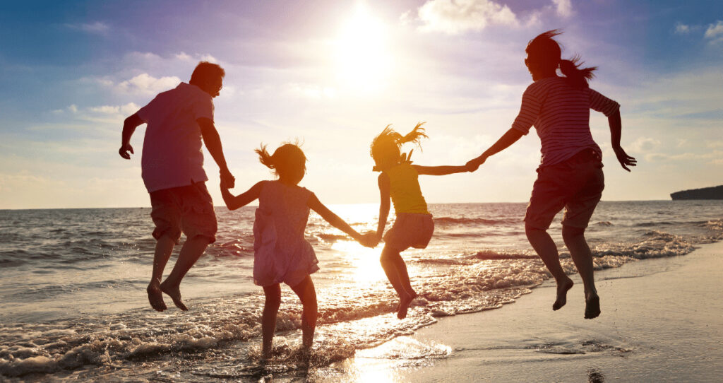 Dois adultos e duas crianças pulando ondas na praia