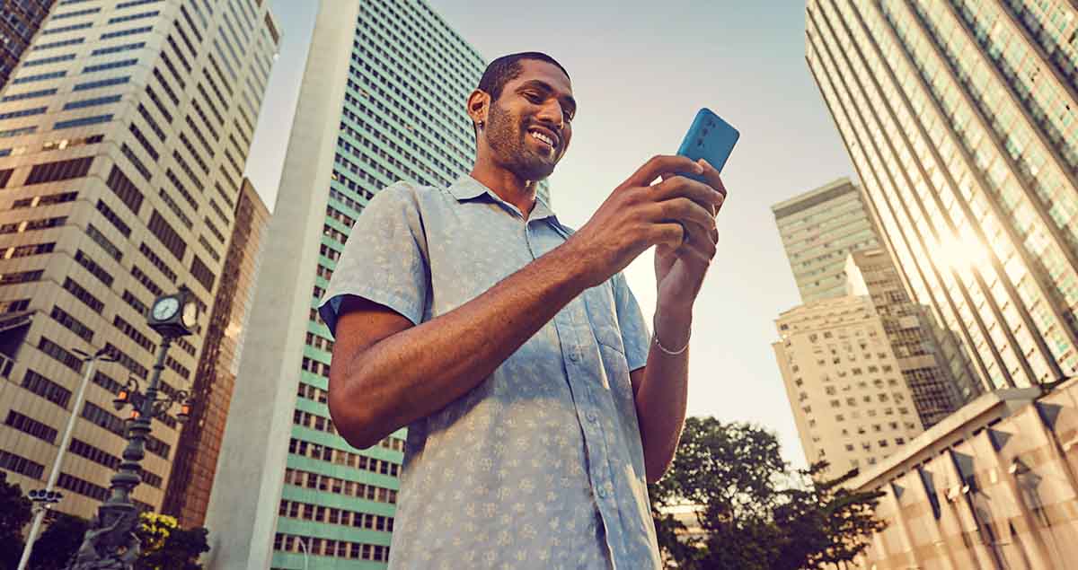 Homem segurando celular na rua e sorrindo