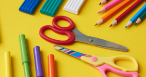Tesouras, canetinhas, borrachas e lápis de cor coloridos sobre fundo amarelo