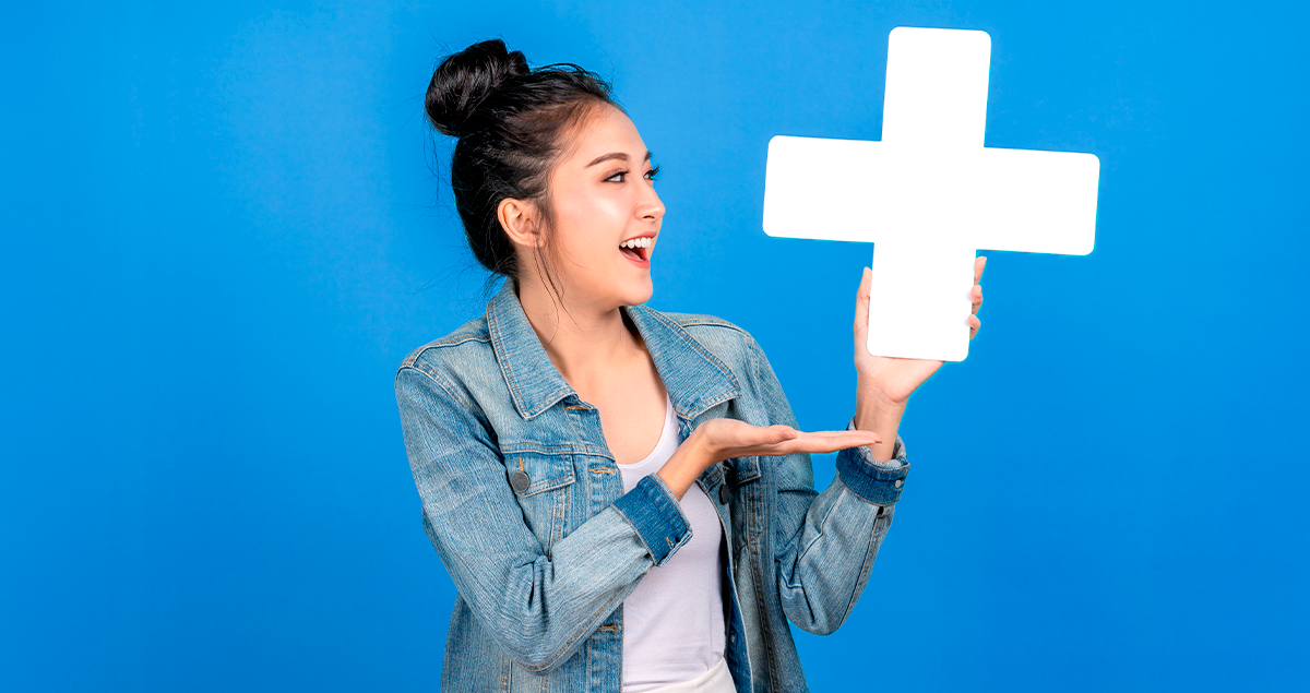 Vale-alimentação: saiba o que é e como funciona este benefício 1 Mulher segurando símbolo de mais e sorrindo em frente a fundo azul