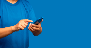 Homem segurando celular em uma mão em frente a fundo azul