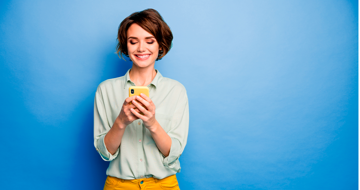 Mulher sorrindo segurando celular nas mãos em frente a fundo azul
