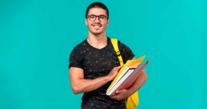 Homem segurando livros sorrindo em frente a fundo verde-água