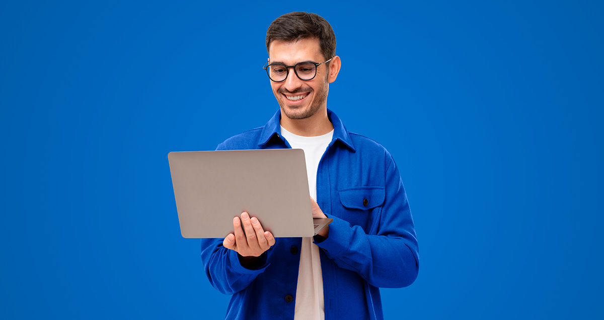 Homem sorrindo em frente a fundo azul e segurando computador