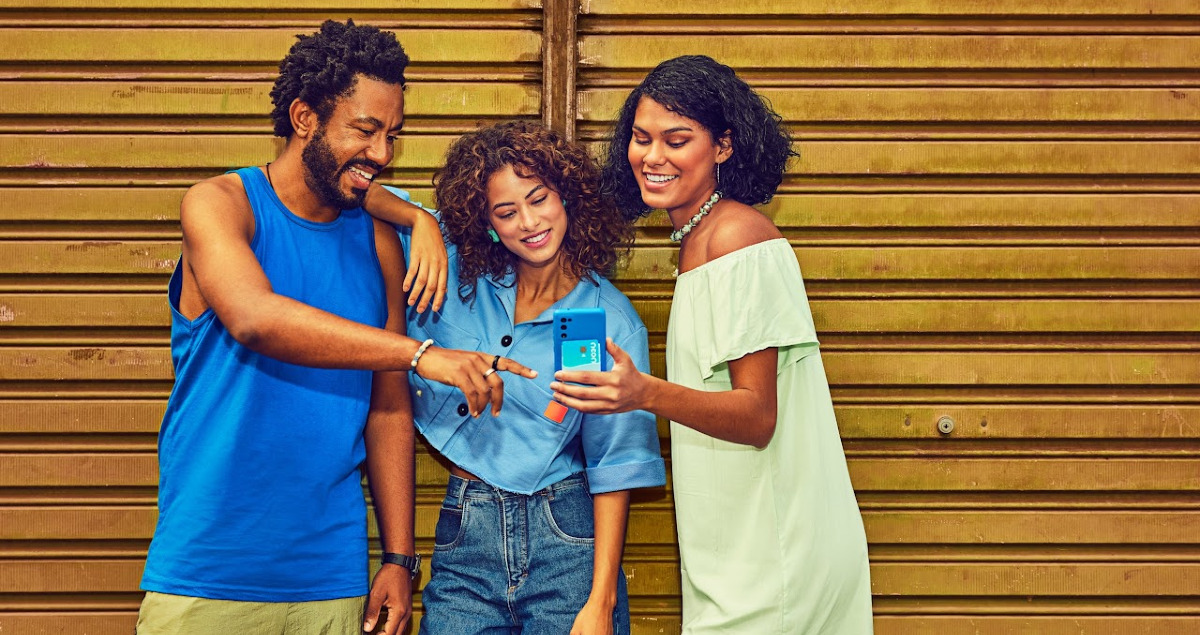 Rendimento Neon: CDB com liquidez diária dá até 113% do CDI 1 Três pessoas olhando para celular em frente a portão amarelo de ferro