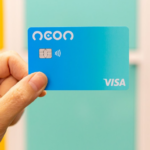 Mão segurando cartão de crédito Neon em frente a fundo colorido