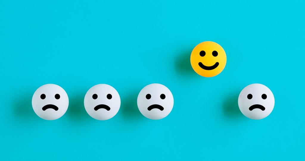 Emojis brancos tristes enfileirados com um emoji feliz amarelo em destaque