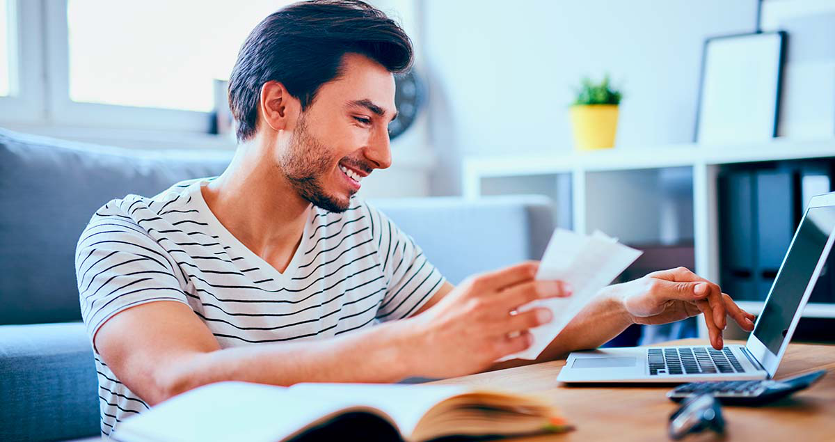 Homem sorrindo segurando papéis em frente a computador