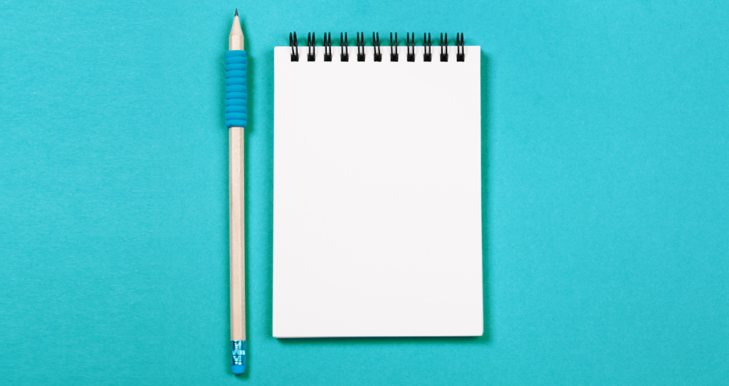 Lápis ao lado de bloco de notas em branco, ambos sobre fundo azul