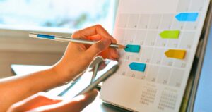 Pessoa escrevendo em calendário marcado com setas coloridas