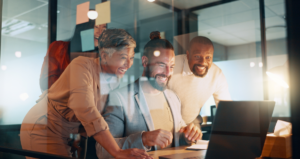 Quatro pessoas sorrindo em volta de mesa com computador