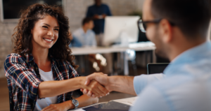 Mulher sorrindo e apertando a mão de um homem em escritório