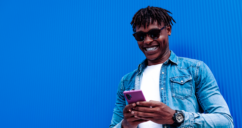 Homem segurando celular na mão e sorrindo em frente a fundo azul