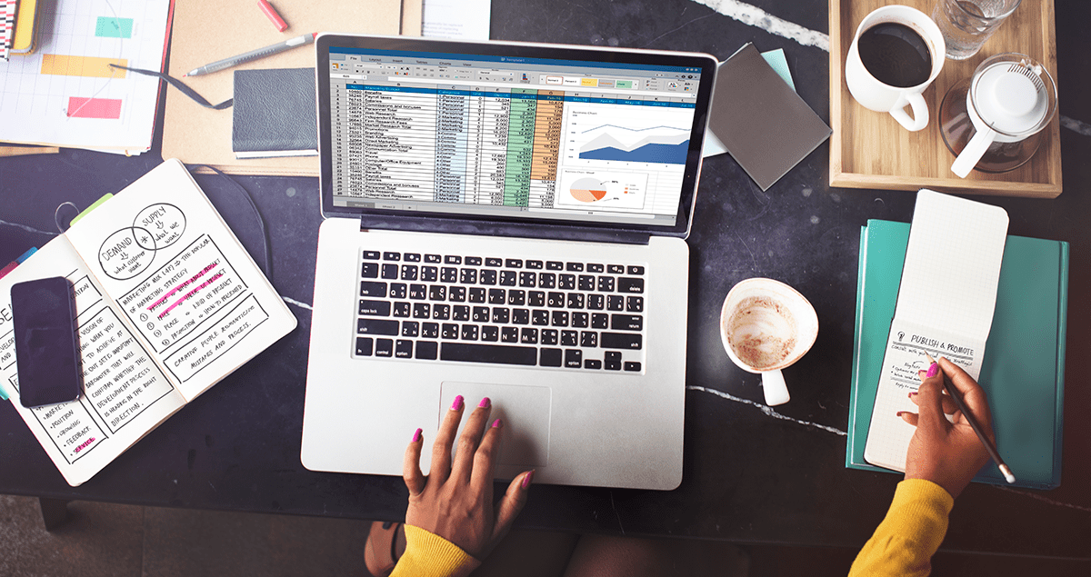 Pessoa em frente a computador em que se vê uma planilha na tela