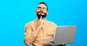 Homem em dúvida segurando computador em frente a fundo azul