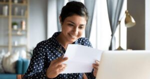Mulher em frente a computador segurando papel e sorrindo