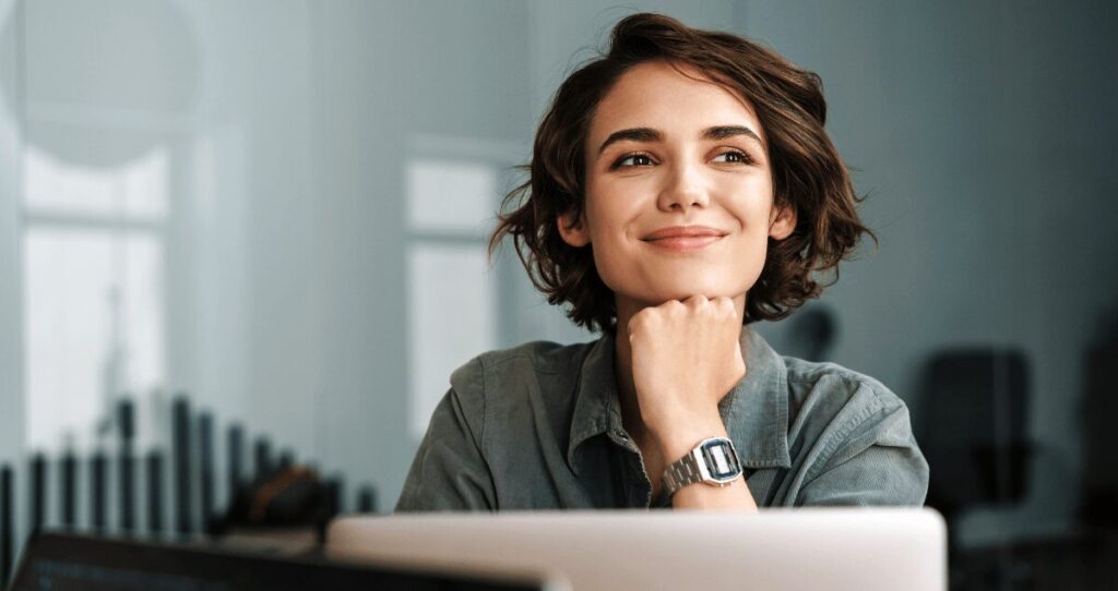 Mulher sorrindo olhando para o lado em frente a computador