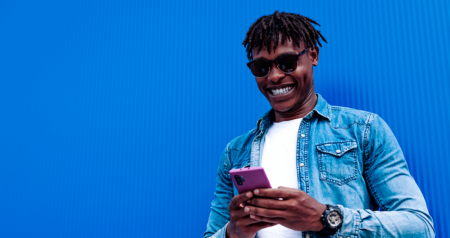 Homem em frente a parede azul sorrindo olhando para celular