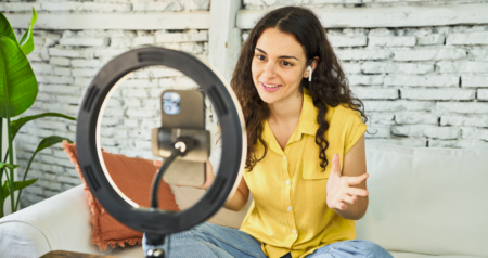 Mulher gravando vídeo com celular em tripé em sala de estar