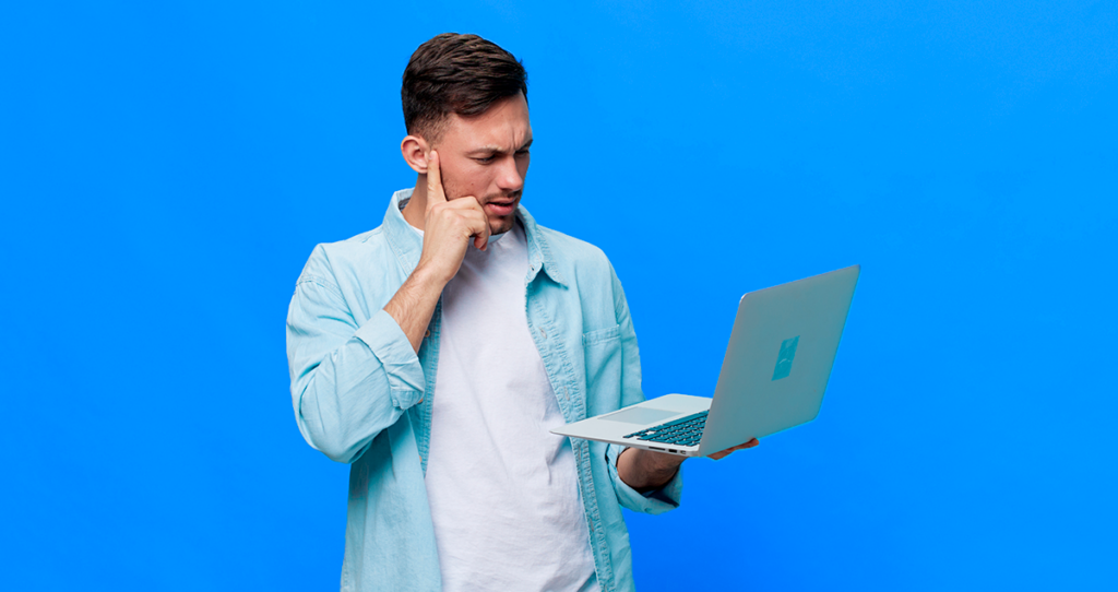 Homem com semblante de dúvida segurando computador nas mãos