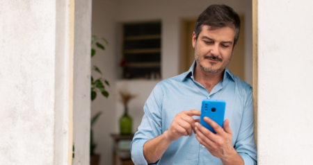 Homem escrevendo em celular em frente de casa