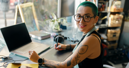 Mulher em frente a computador desenhando em tablet