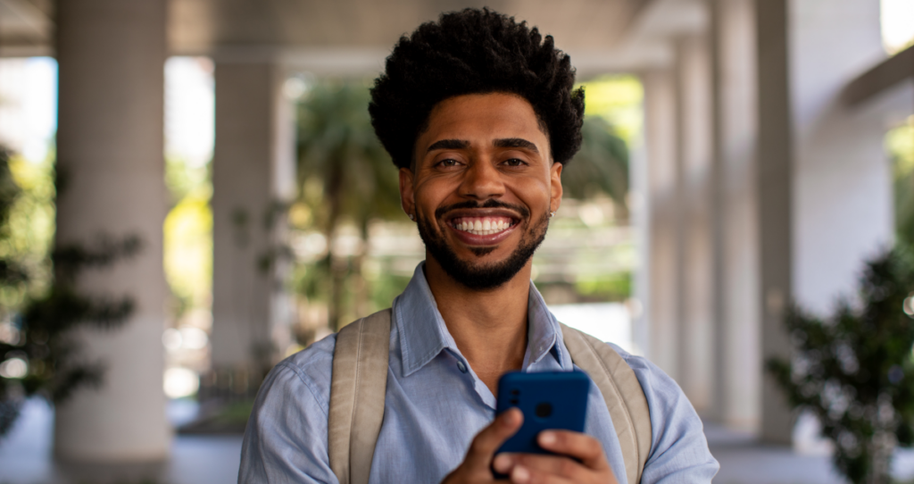 Homem de mochila segurando celular e sorrindo