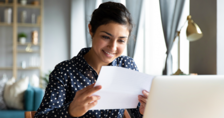 Mulher segurando papel em frente a computador e sorrindo