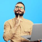 Homem pensativo segurando notebook nas mãos em frente a fundo azul