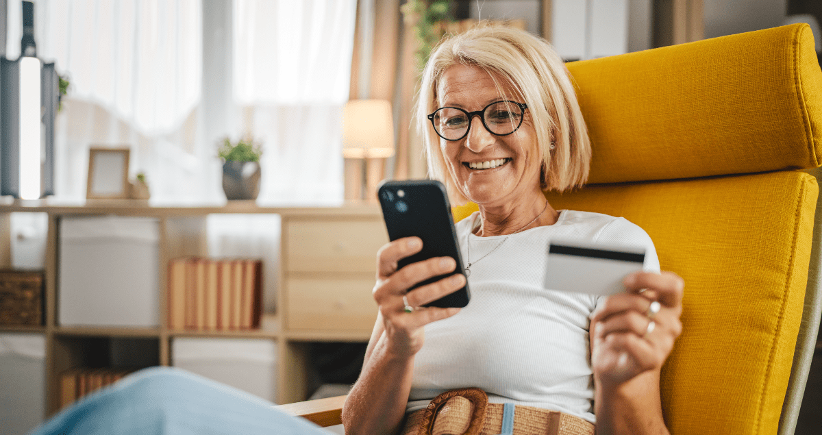 Mulher sentada em poltrona segurando celular em uma mão e cartão em outra