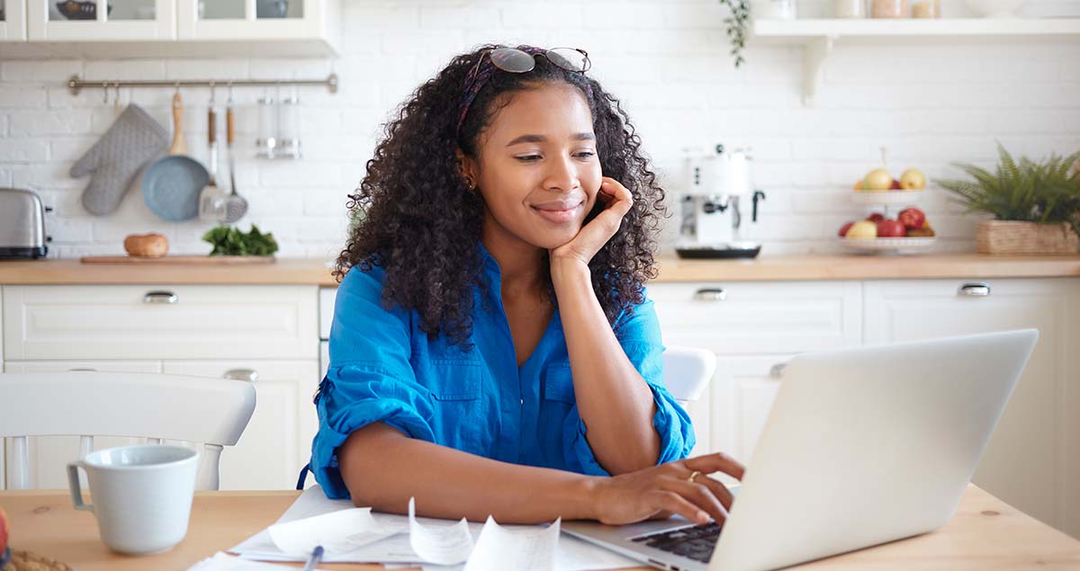 Mulher digitando em computador em cima de mesa de cozinha